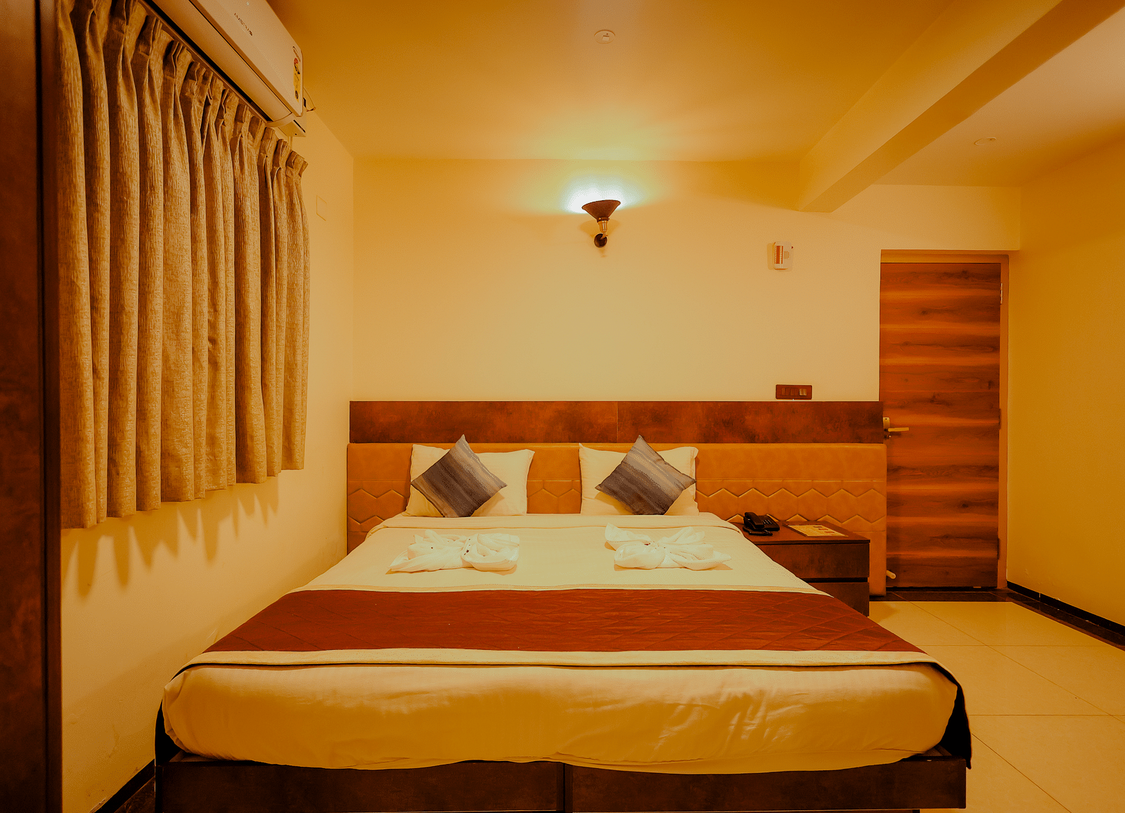 A comfortable bed in a room at Nirantara Resort & Spa, Bengaluru, with warm lighting and wooden furniture.