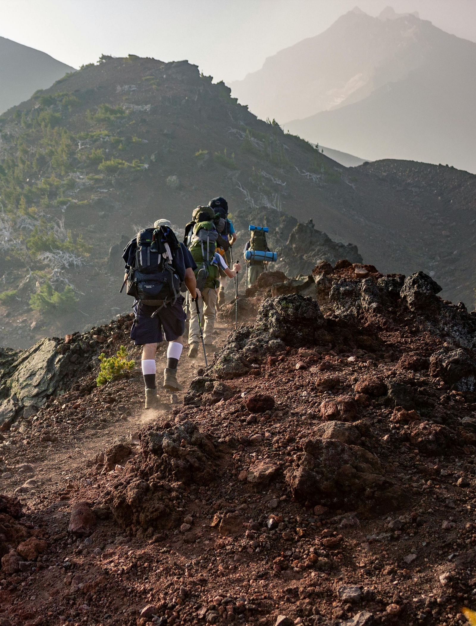 A group of hikers climbing a mountain with other mountains in view.