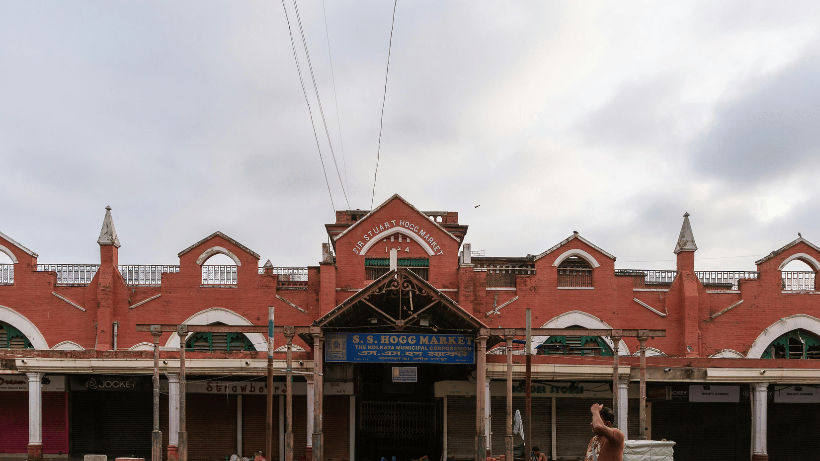 New Market in Kolkata with a person walking in front of it and numerous other people sleeping in front of it