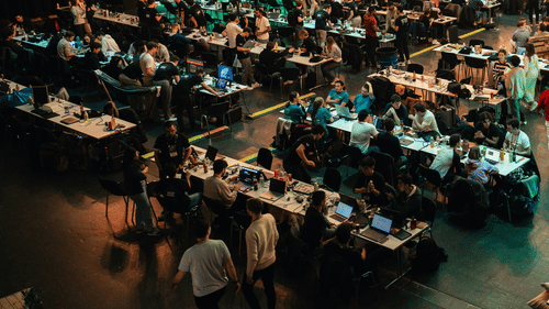 An expo where people are walking around inside a large indoor space in front of participants seated at long tables in various rows