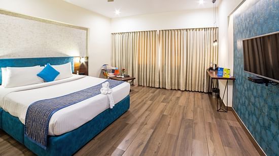 A corner view of the spacious and well-lit hotel room at Icon Boutique Hotel by Bhagini, Domlur, with a bed, a flat-screen TV, and a seating area. with sofa