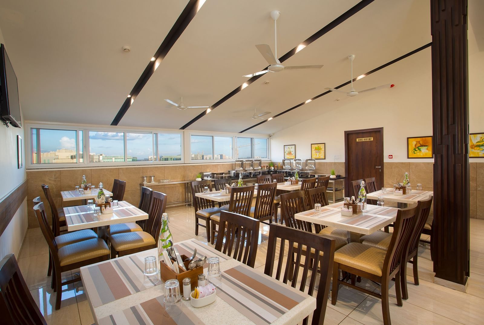 A hotel restaurant with wooden tables and chairs, large windows and ceiling fans - De Venetian by TGI, Brookefield