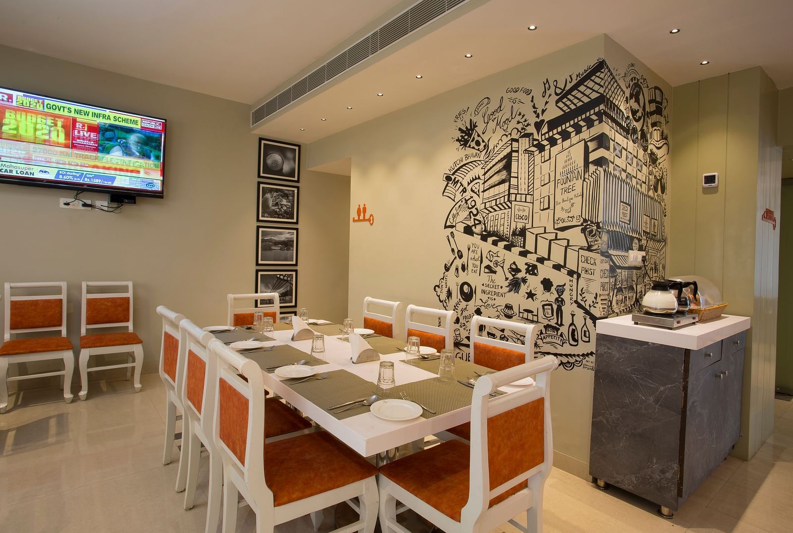 A cosy restaurant corner with a large wall mural, a buffet counter and a flat-screen TV showing news - Hotel Langford Keys by TGI, Shanti Nagar