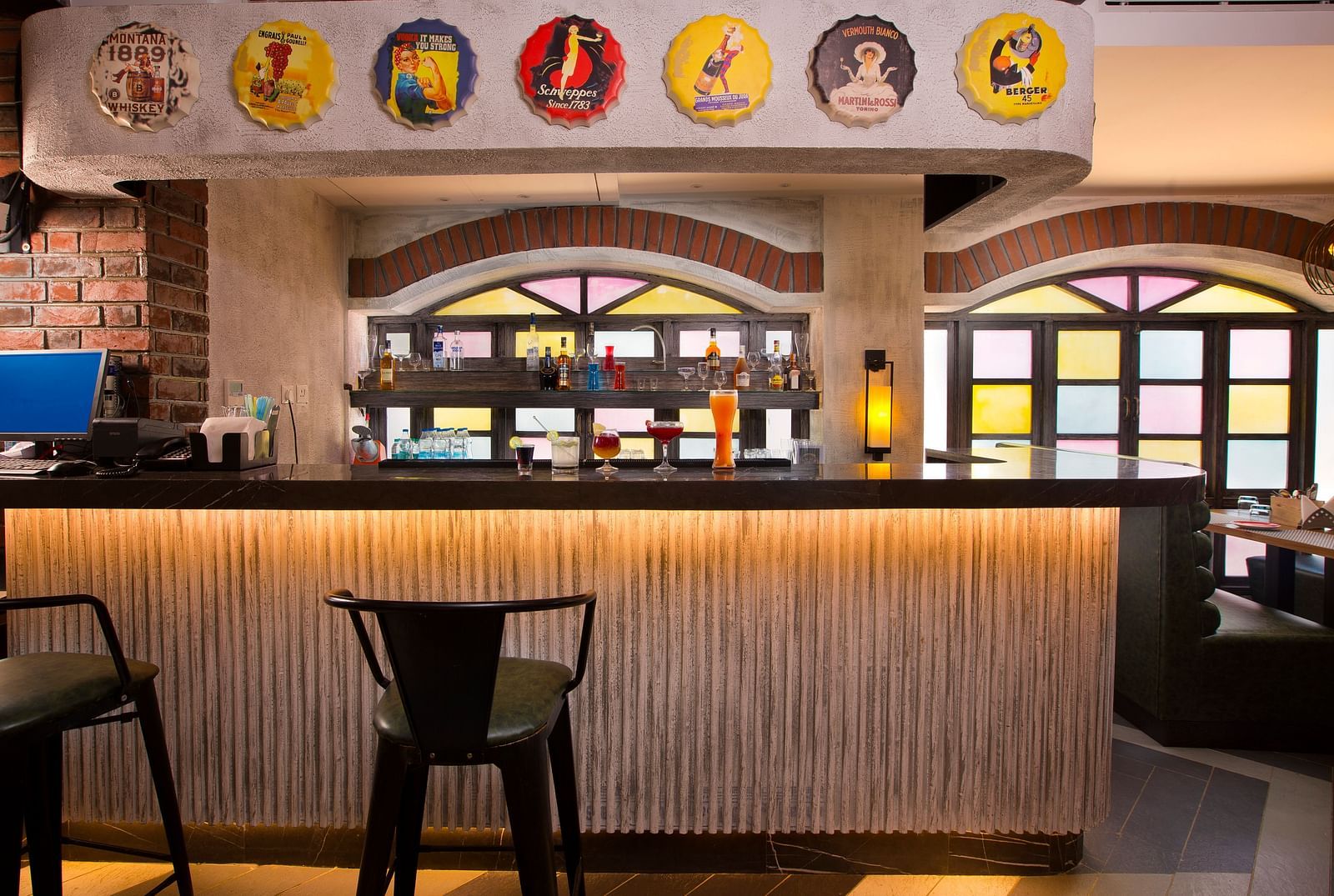 A stylish bar with colourful stained glass windows, a variety of drinks on display and vintage advertisements on the wall - Hotel Southend by TGI - Bommasandra, Bangalore