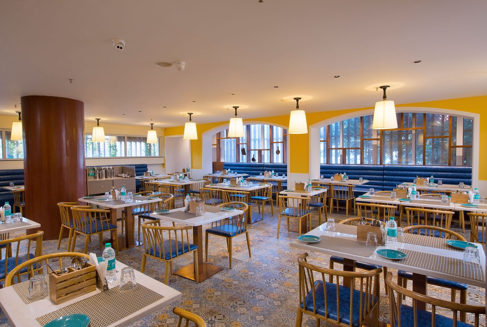 A bright and inviting restaurant interior with yellow walls, pendant lights and blue booth seating - Hotel Southend by TGI - Bommasandra, Bangalore