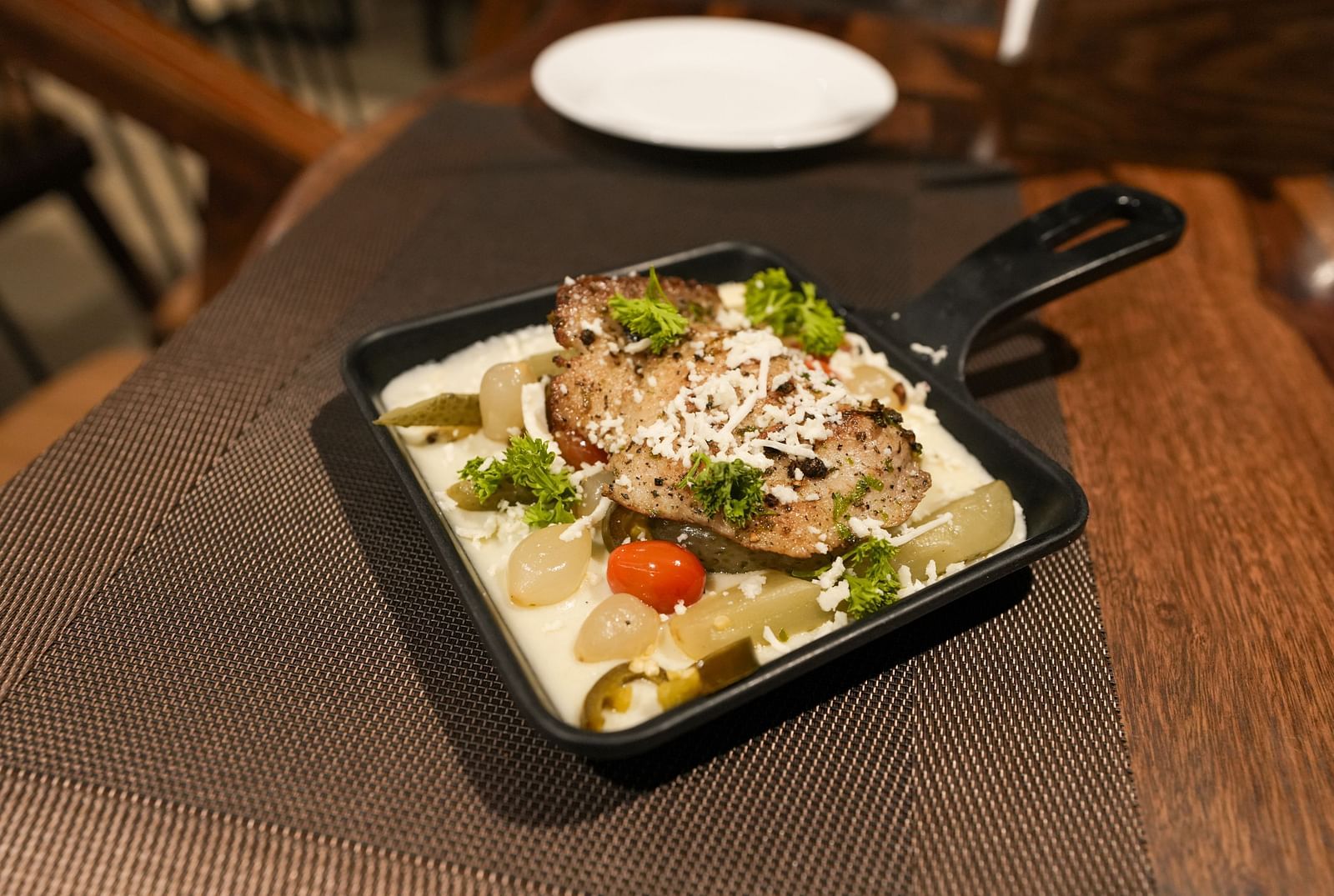 Side view of creamy pasta with grilled chicken and vegetables in a black skillet on a table at TGI Livancia Hillside, JC Nagar, Mysore