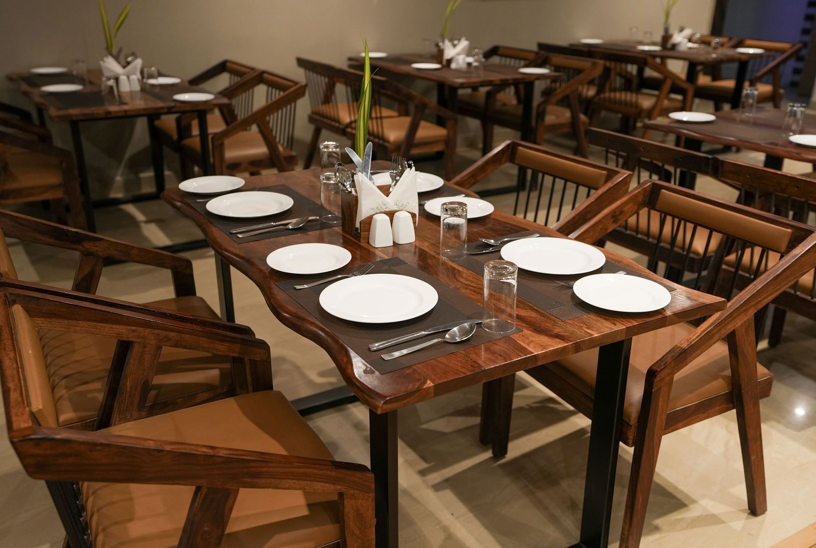 Close-up of a wooden table set for six with curved edges and modern wooden chairs at TGI Livancia Hillside, JC Nagar, Mysore