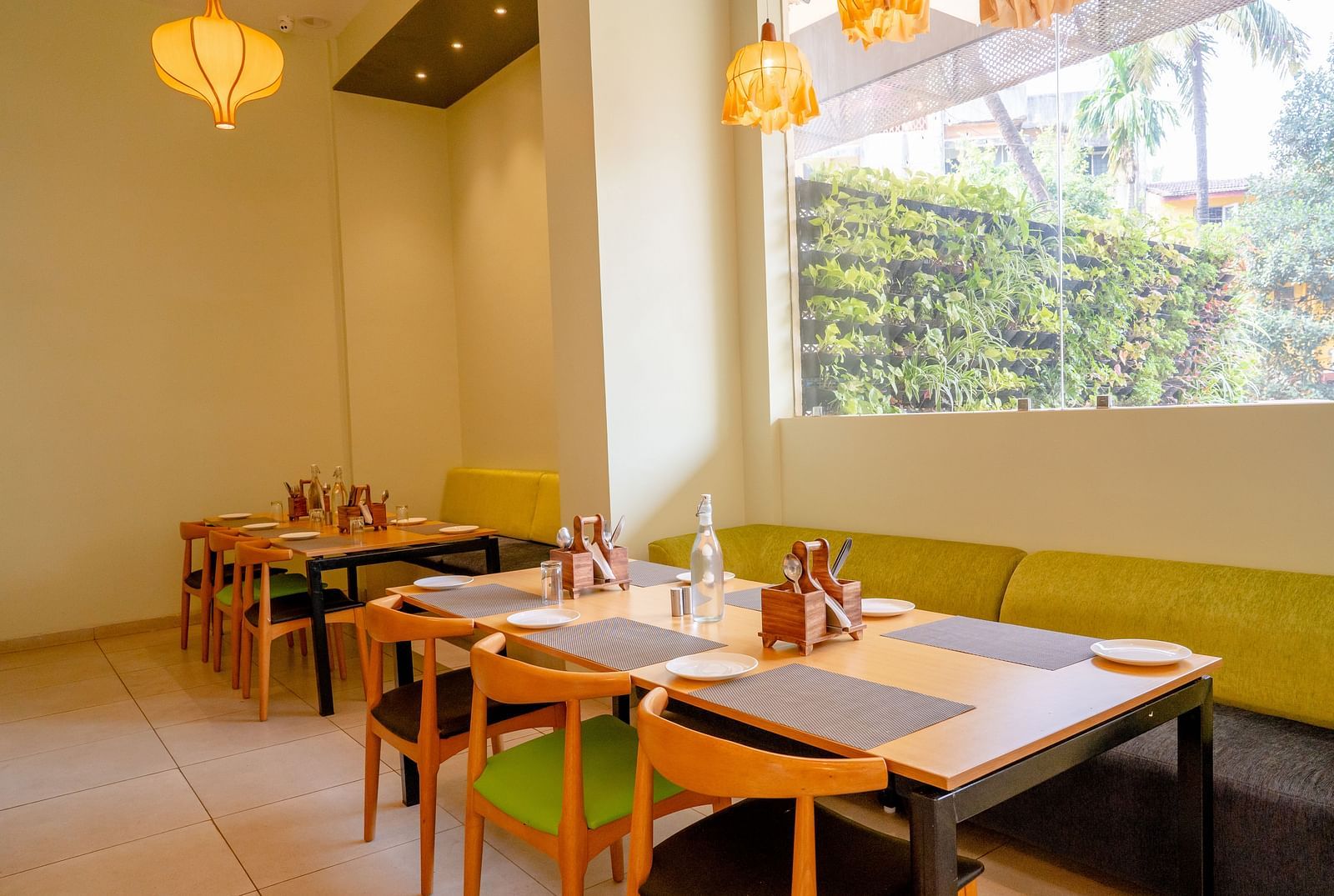 A neatly arranged restaurant dining area with tables, chairs and pendant lights- TGI Ameya Grand, Goa