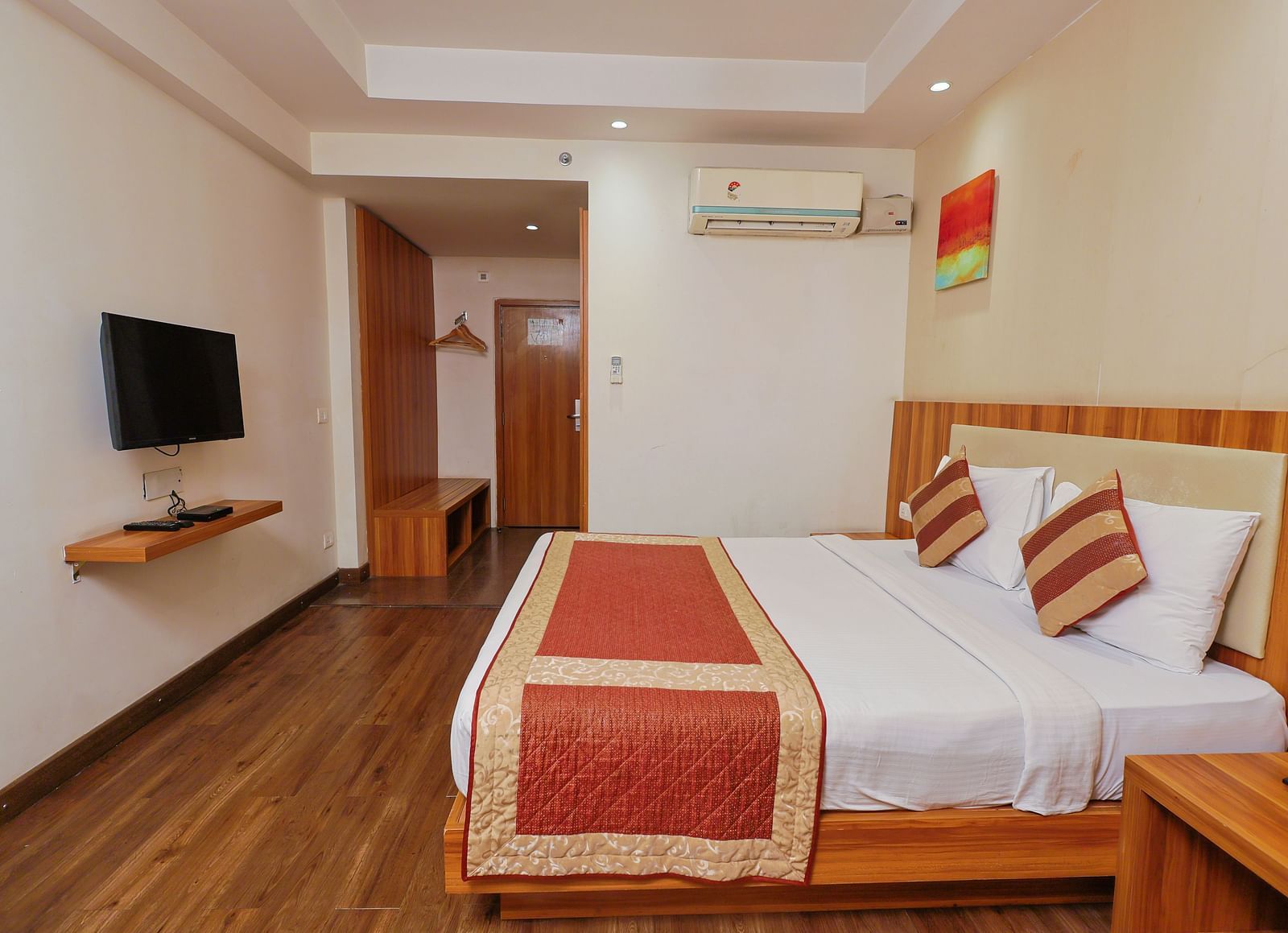 A wide angle side view of the bedroom with plushy bed and TV a small corridor haeding towards to door at Le Roi udaipur