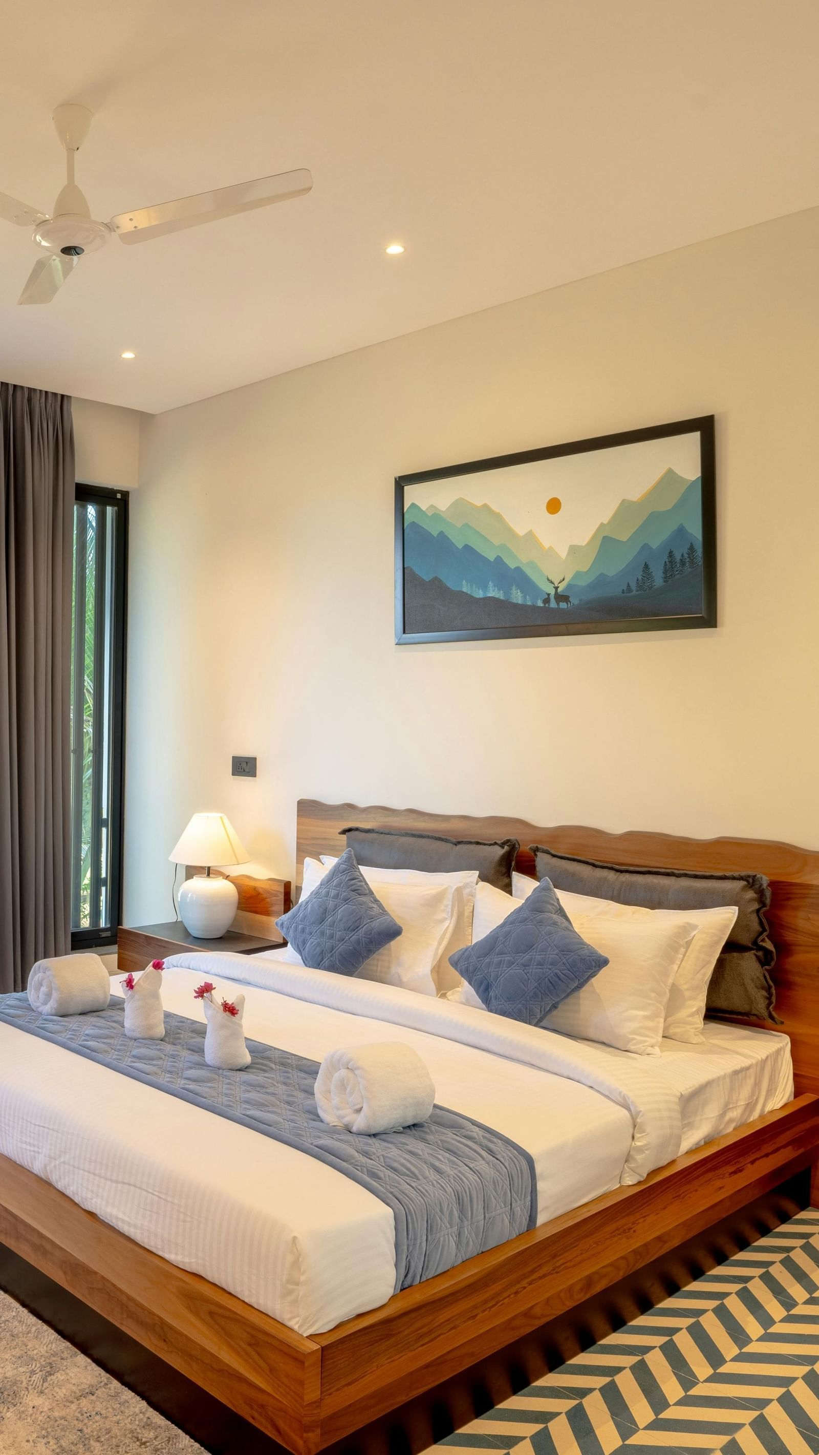 A cosy room featuring a neatly made bed, matching side tables, a large window that fills the space with natural light, and contemporary furnishings