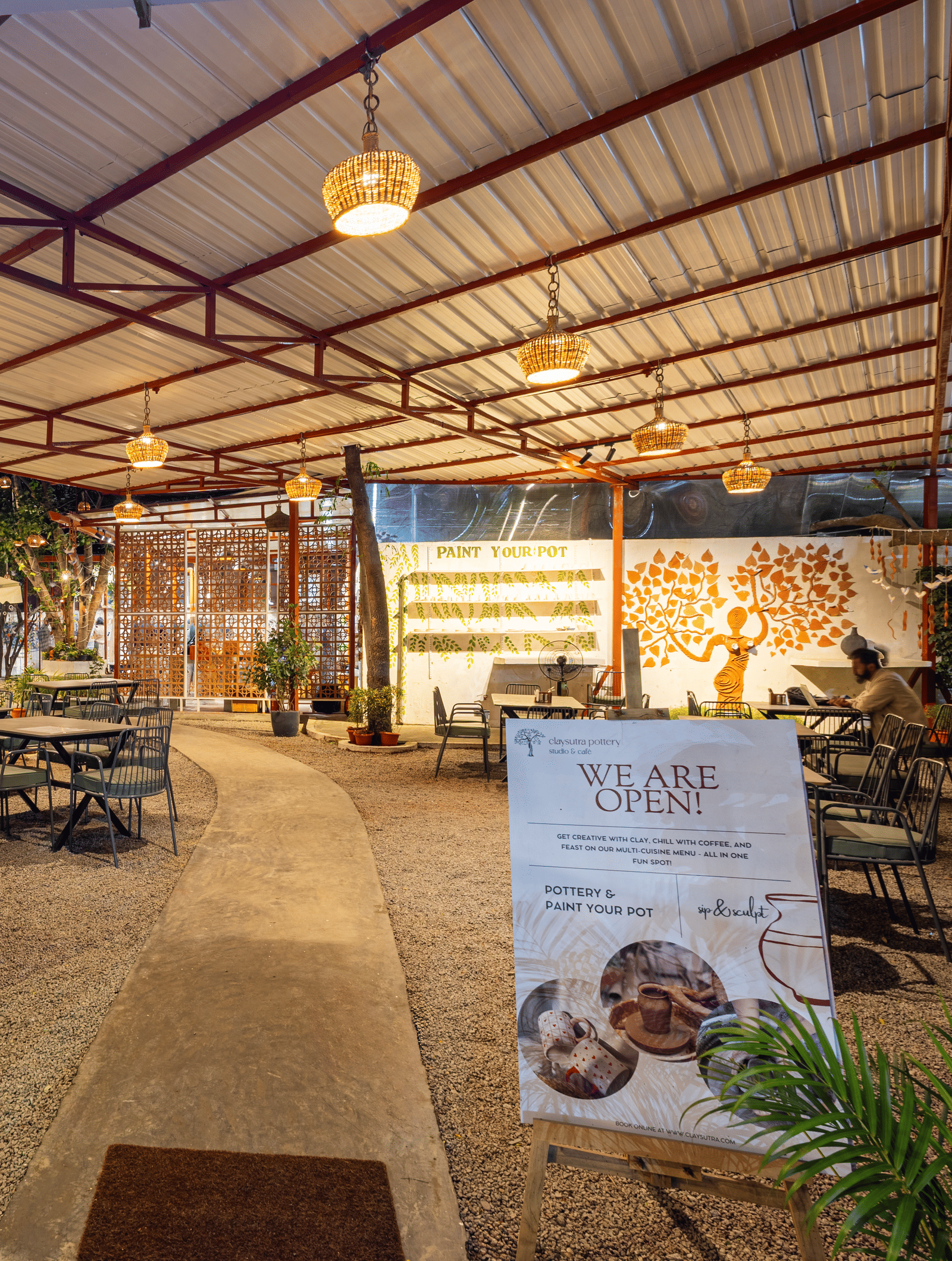 Claysutra Cafe & Restaurant at Kove Smart Stays seen during a darker time of the day, with ambient lighting, outdoor seating, and an overhead shed.