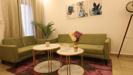 A living room, featuring an olive green sofa, 2 round white coffee tables on a purple rug, and a large tripod floor lamp | Perfectstayz Value Homes, Mussoorie
