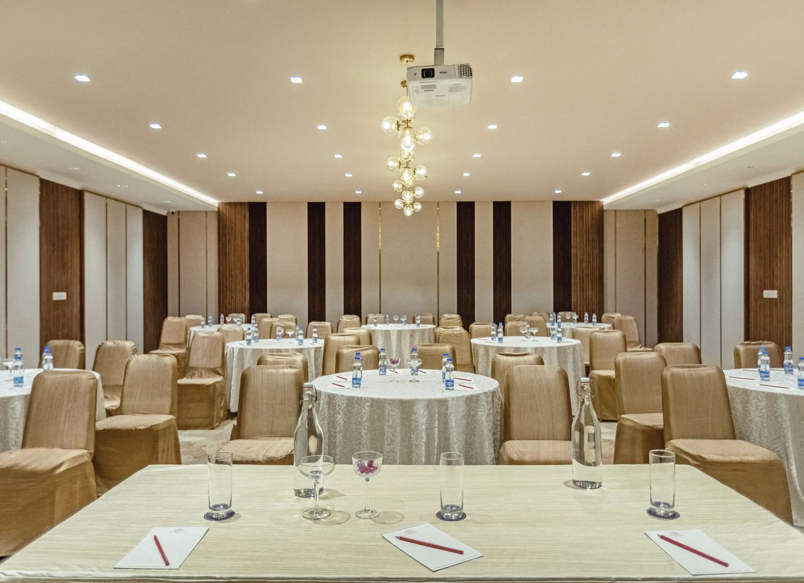 Banquet hall at Mango Hill Central, Chennai, with round tables and chairs arranged for a meeting or event. A projector hangs from the ceiling.