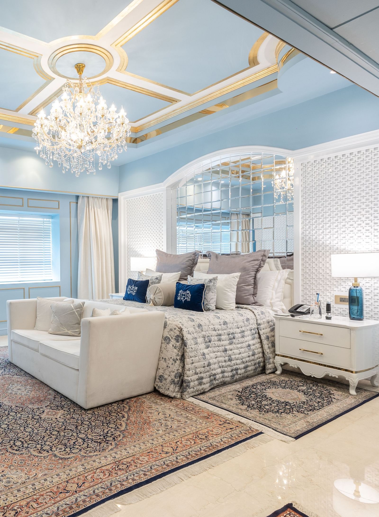 An image of a suite with a large bed and a sofa placed in front of a television and a chandelier hanging from the ceiling