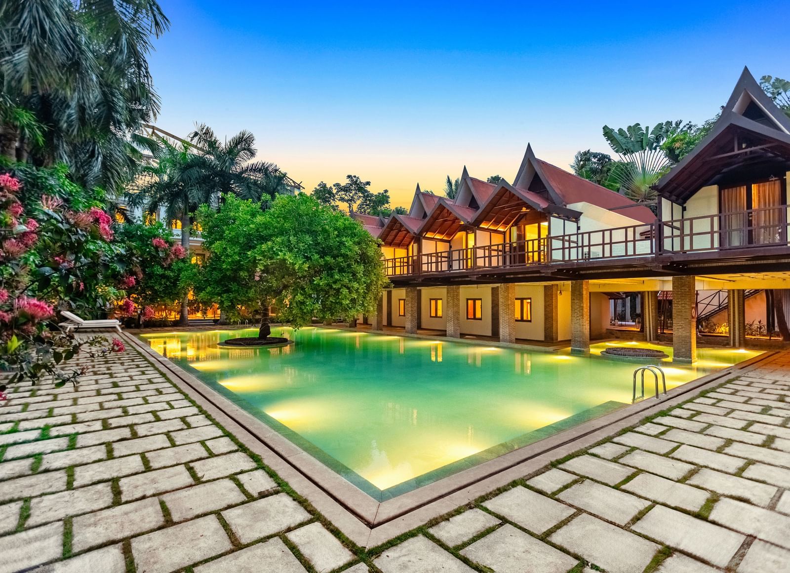 Twilight descends over the beautifully lit pool and traditional villas at Mango Hill Auroville, Pondicherry.