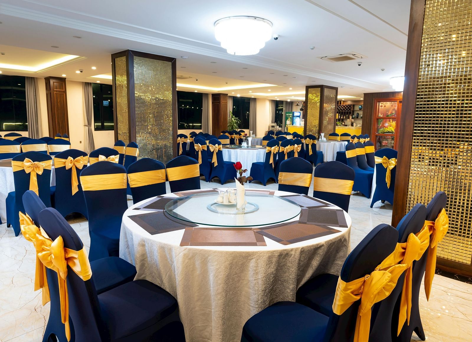 Elegant event space featuring round tables with floral arrangements, blue and gold decorated chairs, and decorative columns