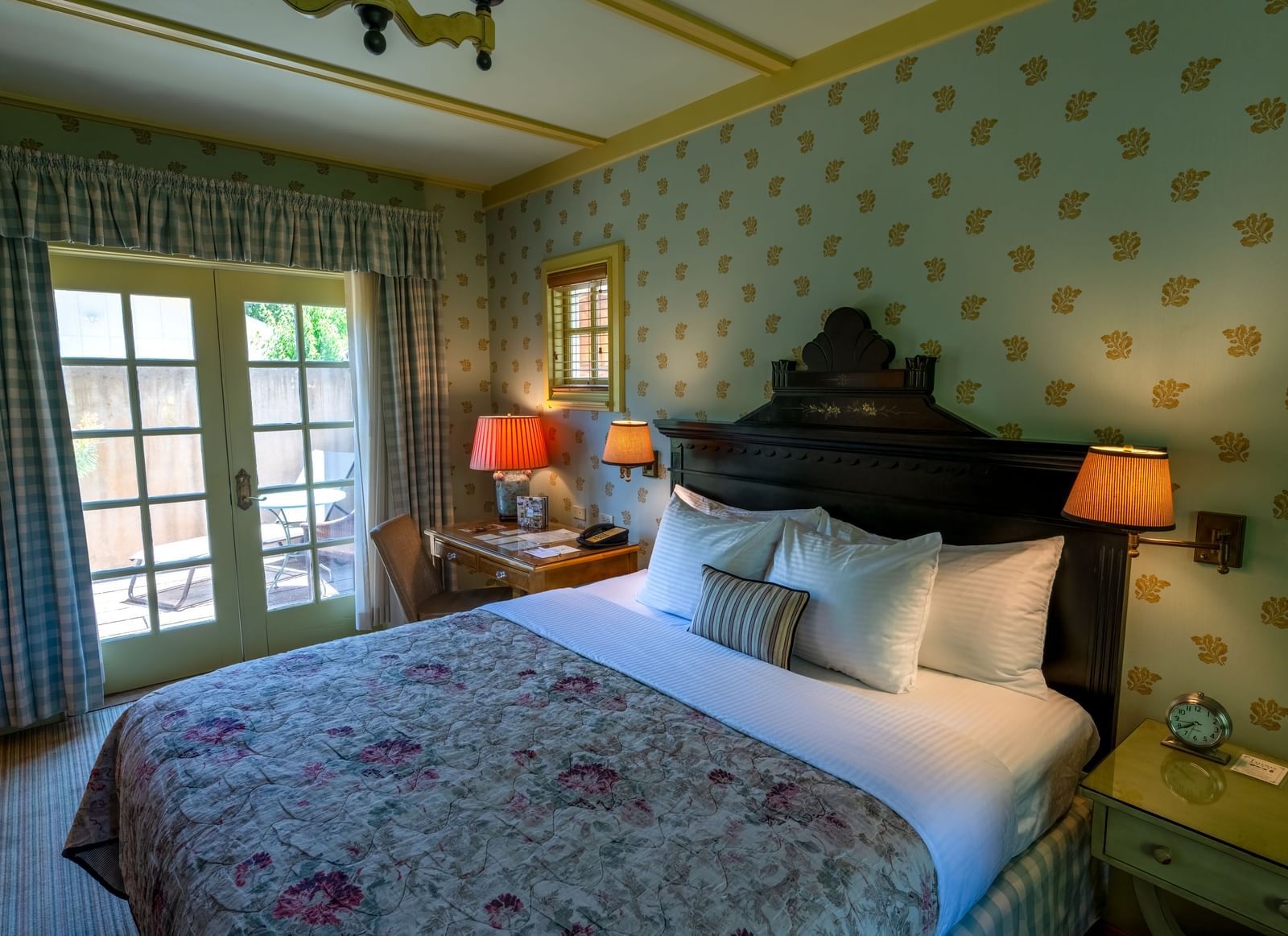 A luxurious bedroom with a large comfortable bed, richly patterned walls, and elegant lamps by the windows at The Tallman Hotel.