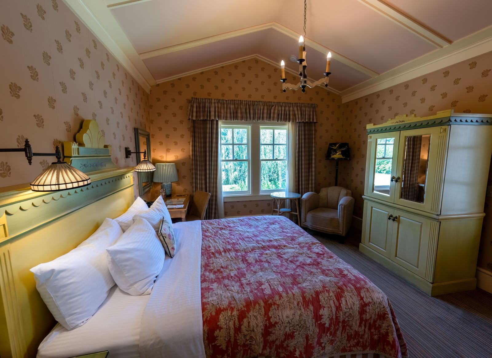 A spacious hotel bedroom with a large bed, elegant red and white patterned bedding, and antique furniture at The Tallman Hotel.