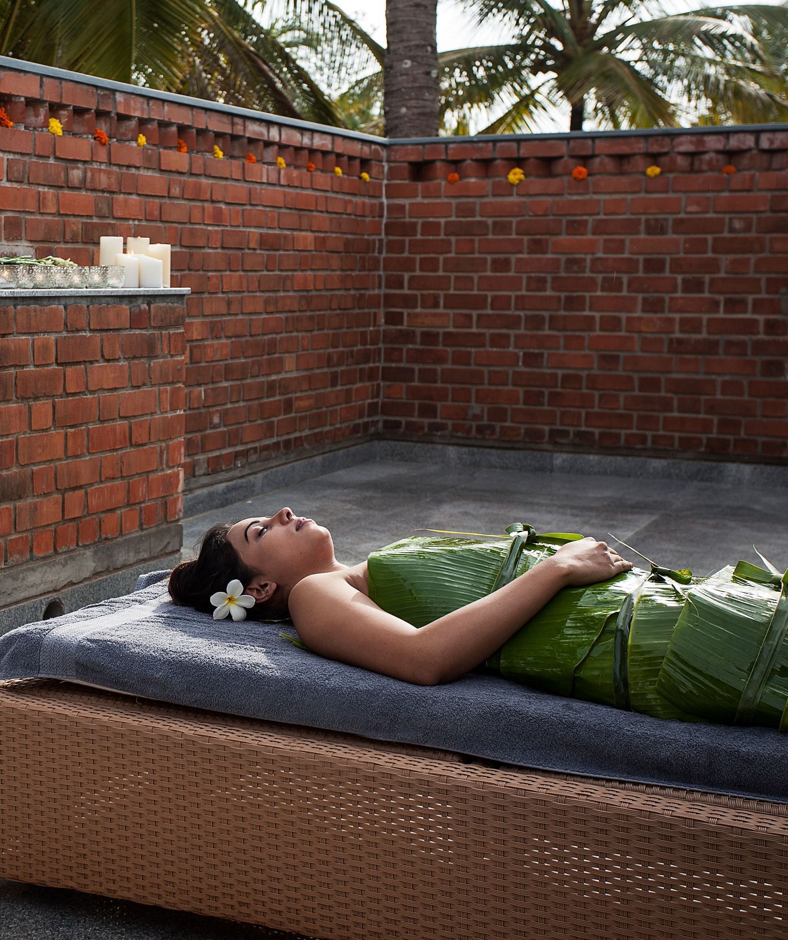 Person lying on a massage table outdoors, brick wall, spa treatment - Shreyas Retreat