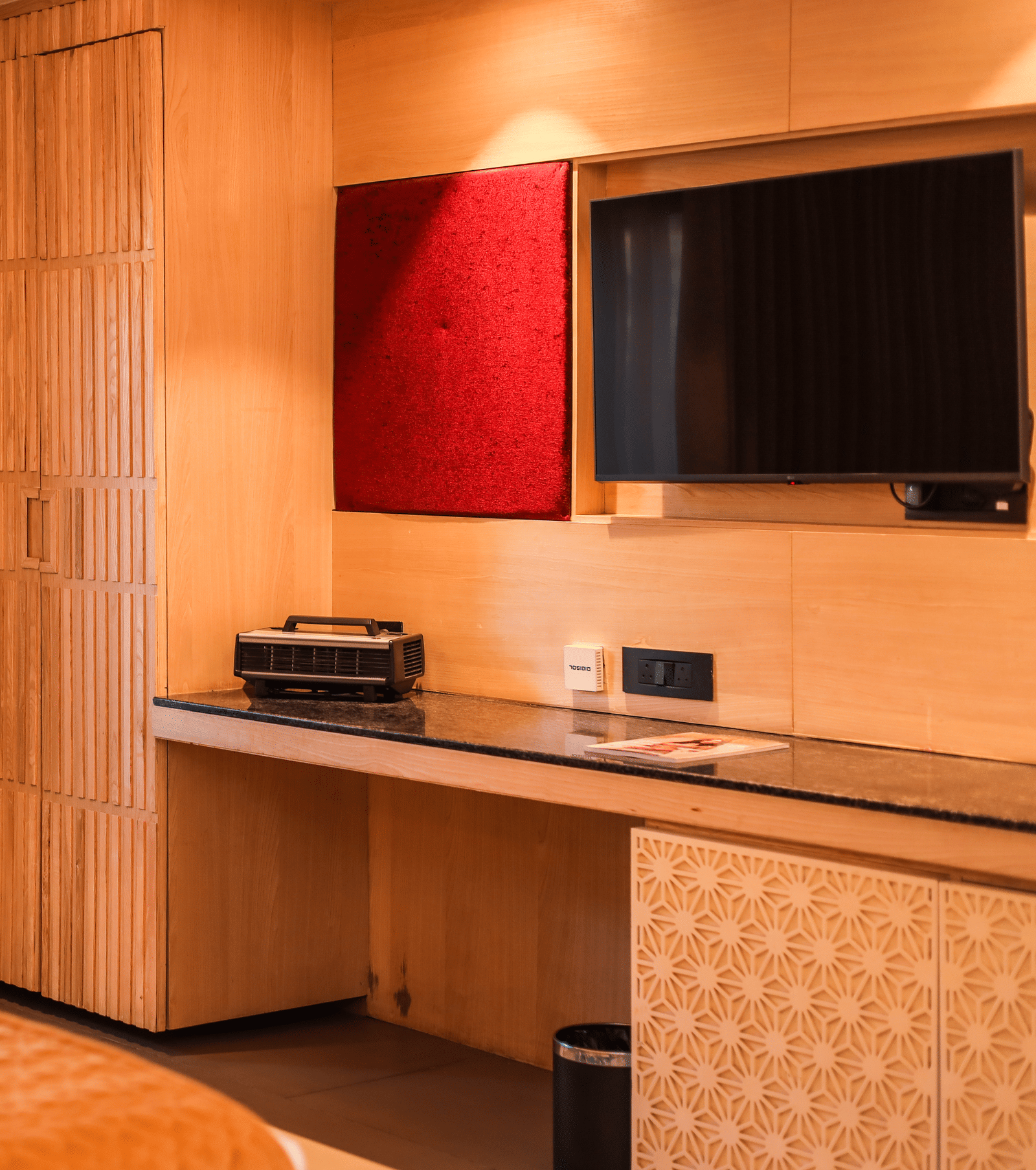 A room with a bed, seating, a desk, mounted television and storage unit at Ananta Spa & Resort, Jaipur.