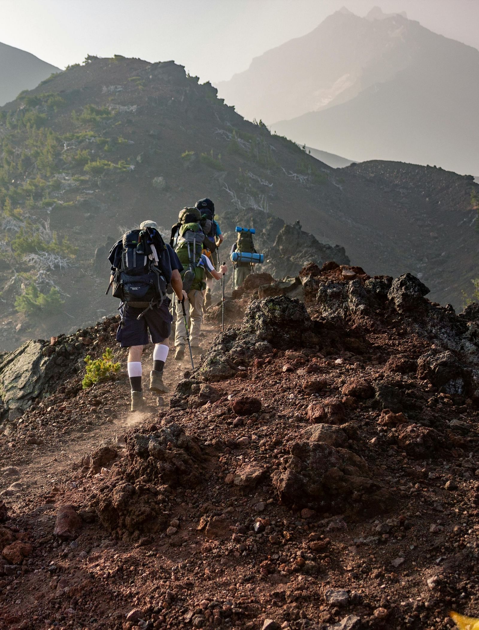 A group of hikers climbing a mountain with other mountains in view.
