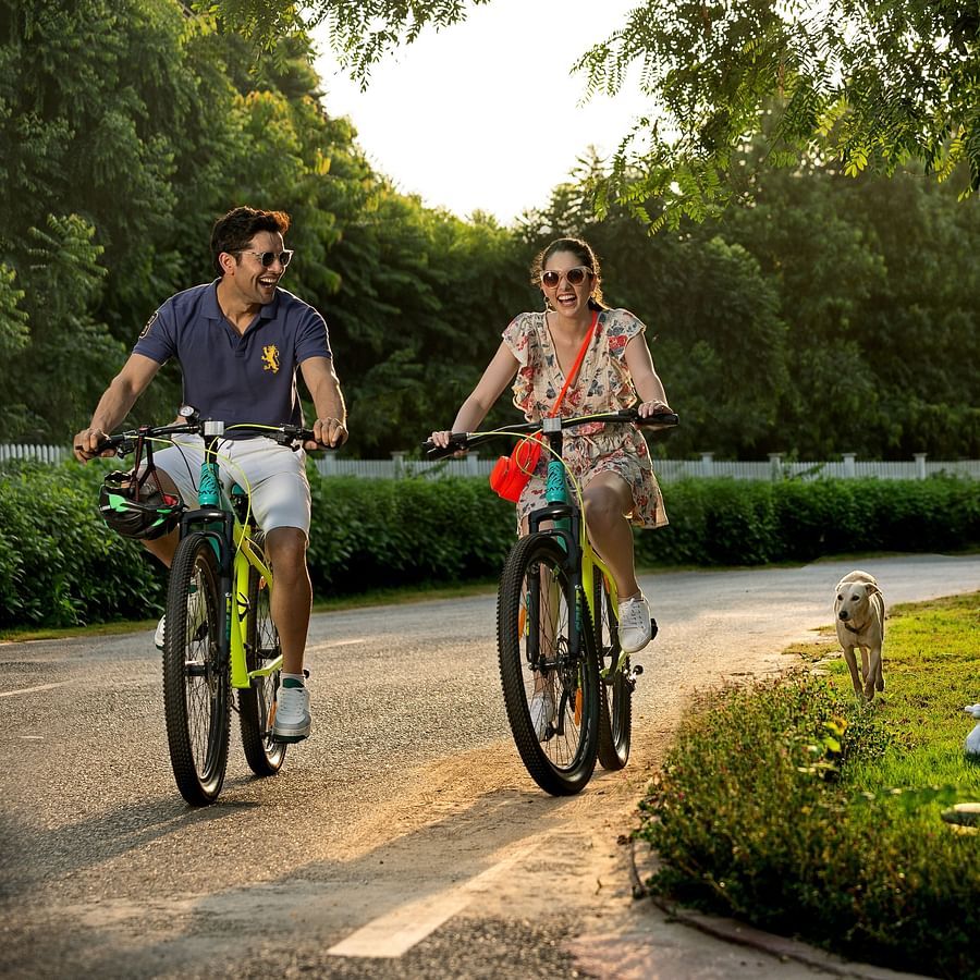 a couple cycling on a stone pathway next to nature and trees with the sun shining from behind them at this Romantic Getaways Delhi - Heritage Village Resort & Spa, Manesar