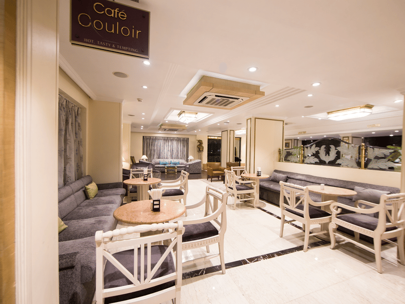 Cafe Couloir at Hotel Bawa International, Vile Parle featuring a dining area with couch and sofa chairs with tables in each setting.