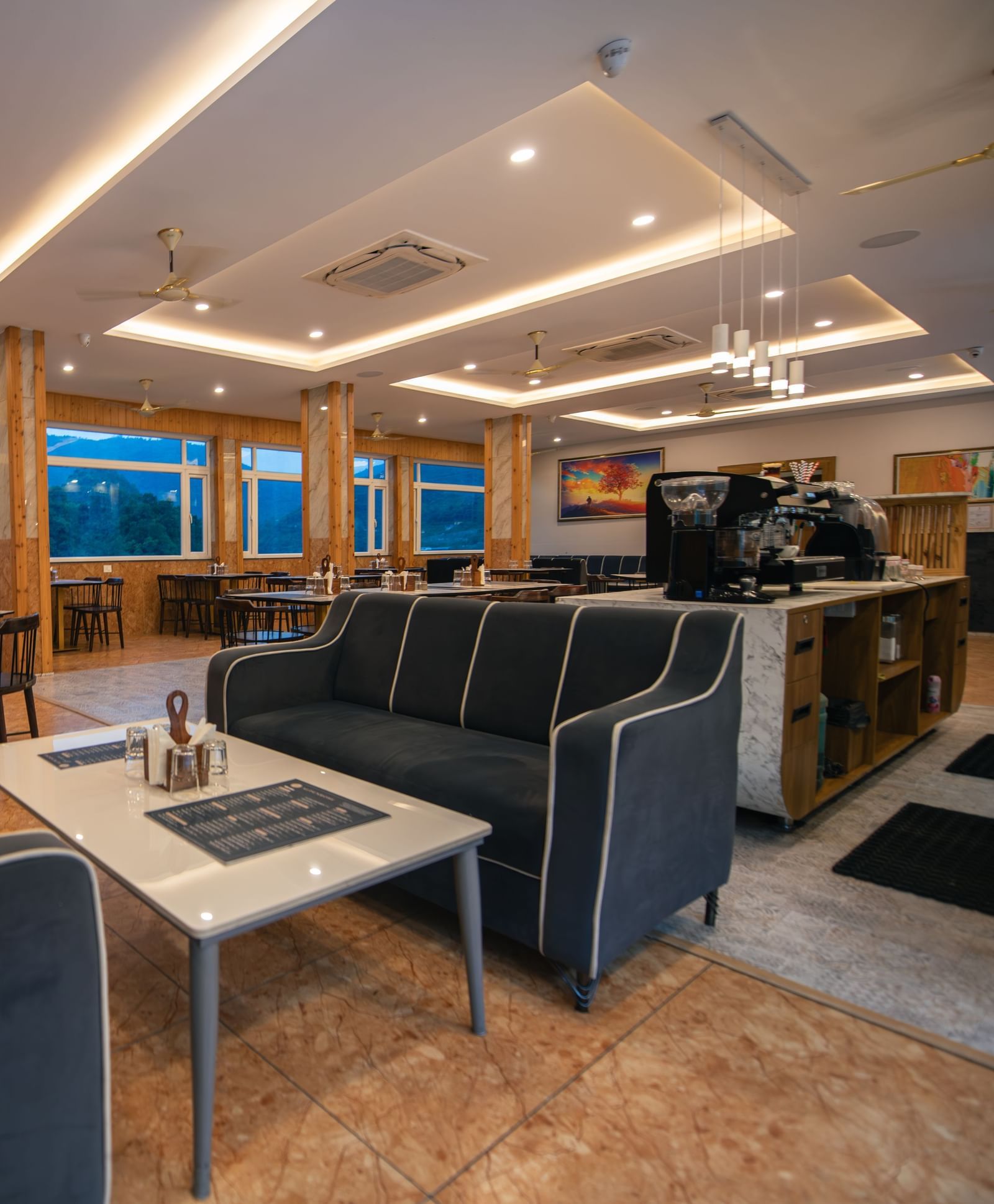A restaurant at The Tattva Devaprayag with dark grey couches and a coffee table.
