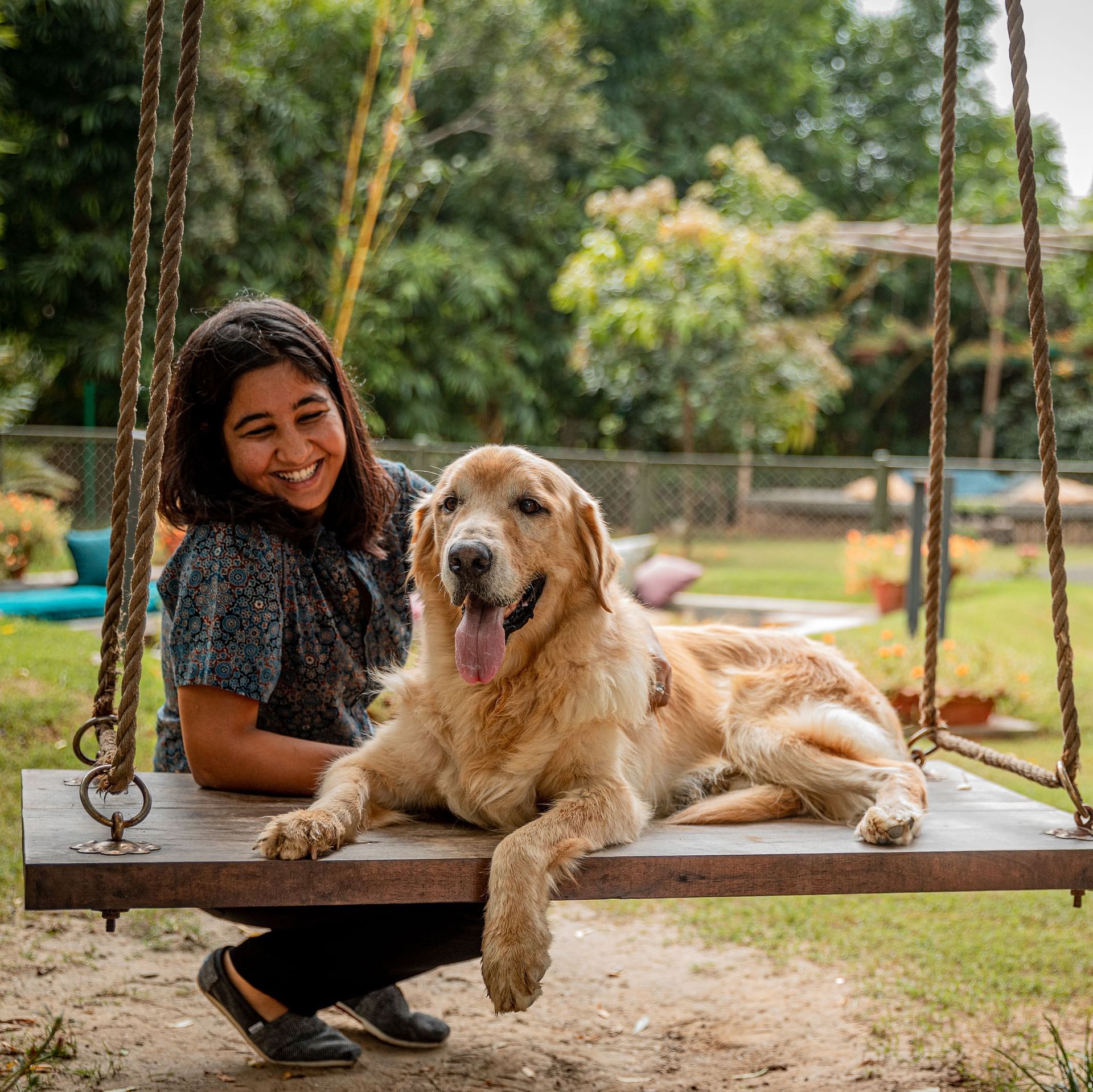 A female and a dog sitting on the large outdoor swing with a lawn area in the backdrop at Karma Chalets.