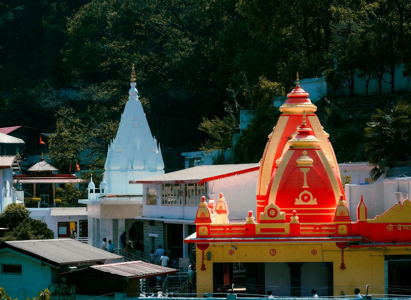 A brightly coloured Hindu temple with a red and white spire, nestled among greenery.