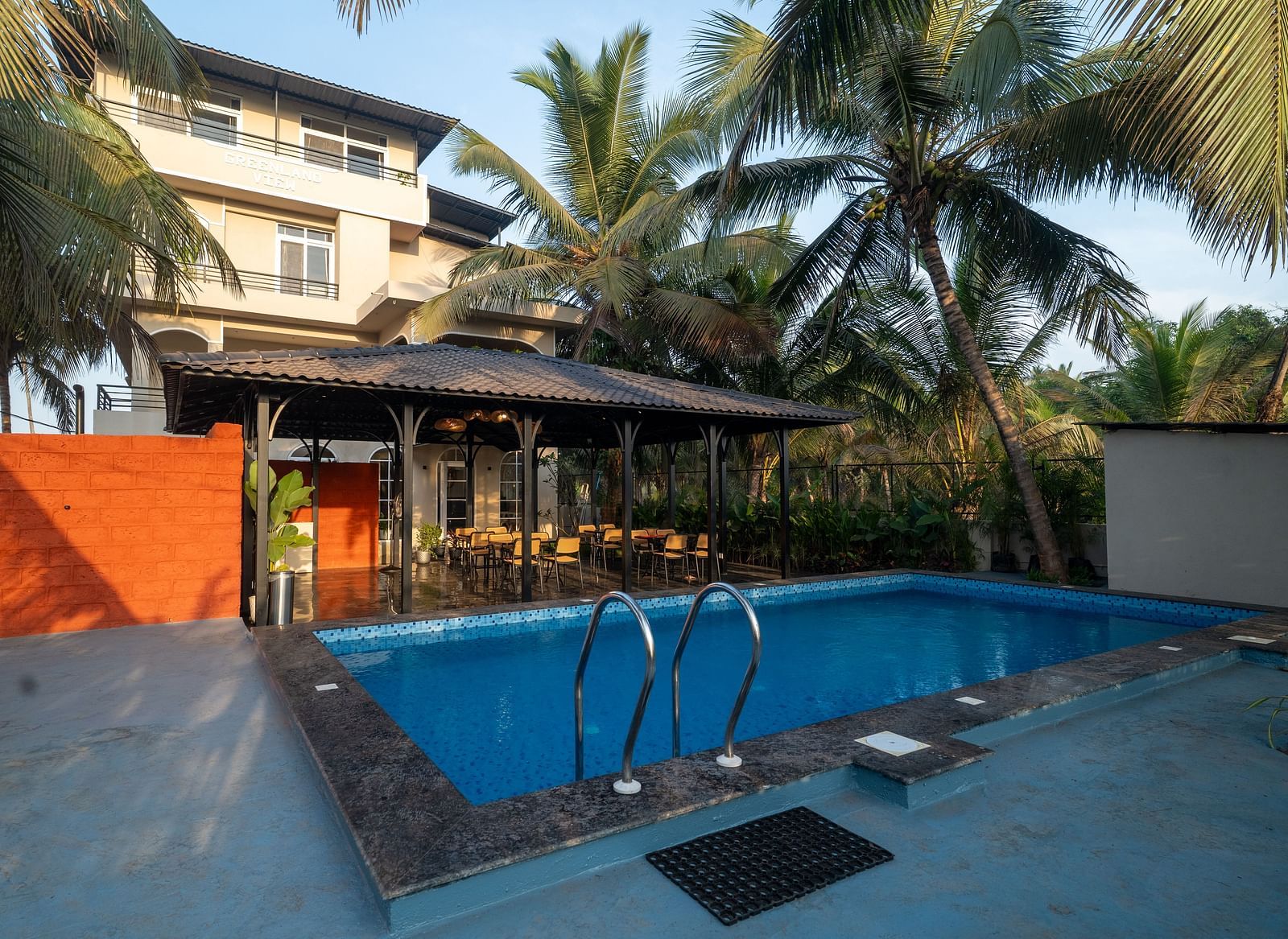 Outdoor swimming pool surrounded by palm trees, adjacent to a covered open-air seating area and Kseemya in the background.