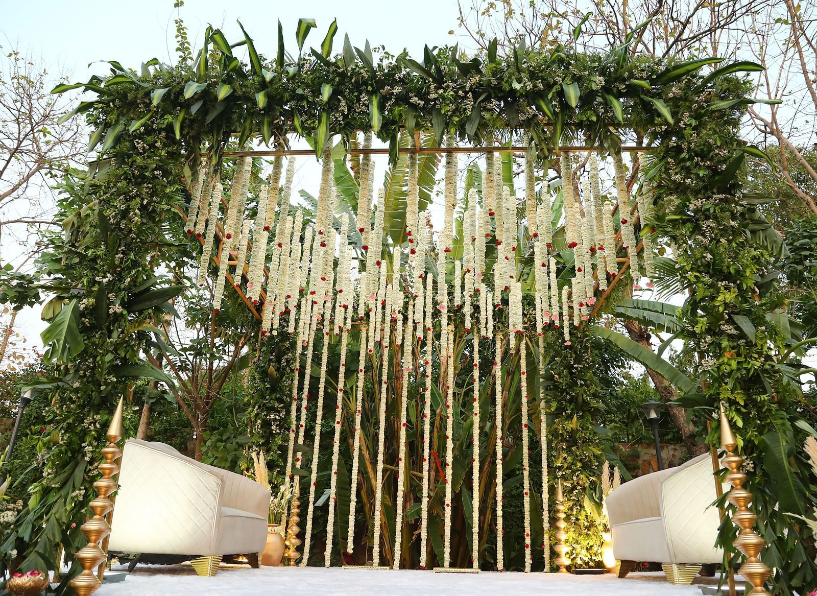 Vertical floral backdrop at Tisya Farms, Gurgaon with hanging garlands and two white chairs on either side.