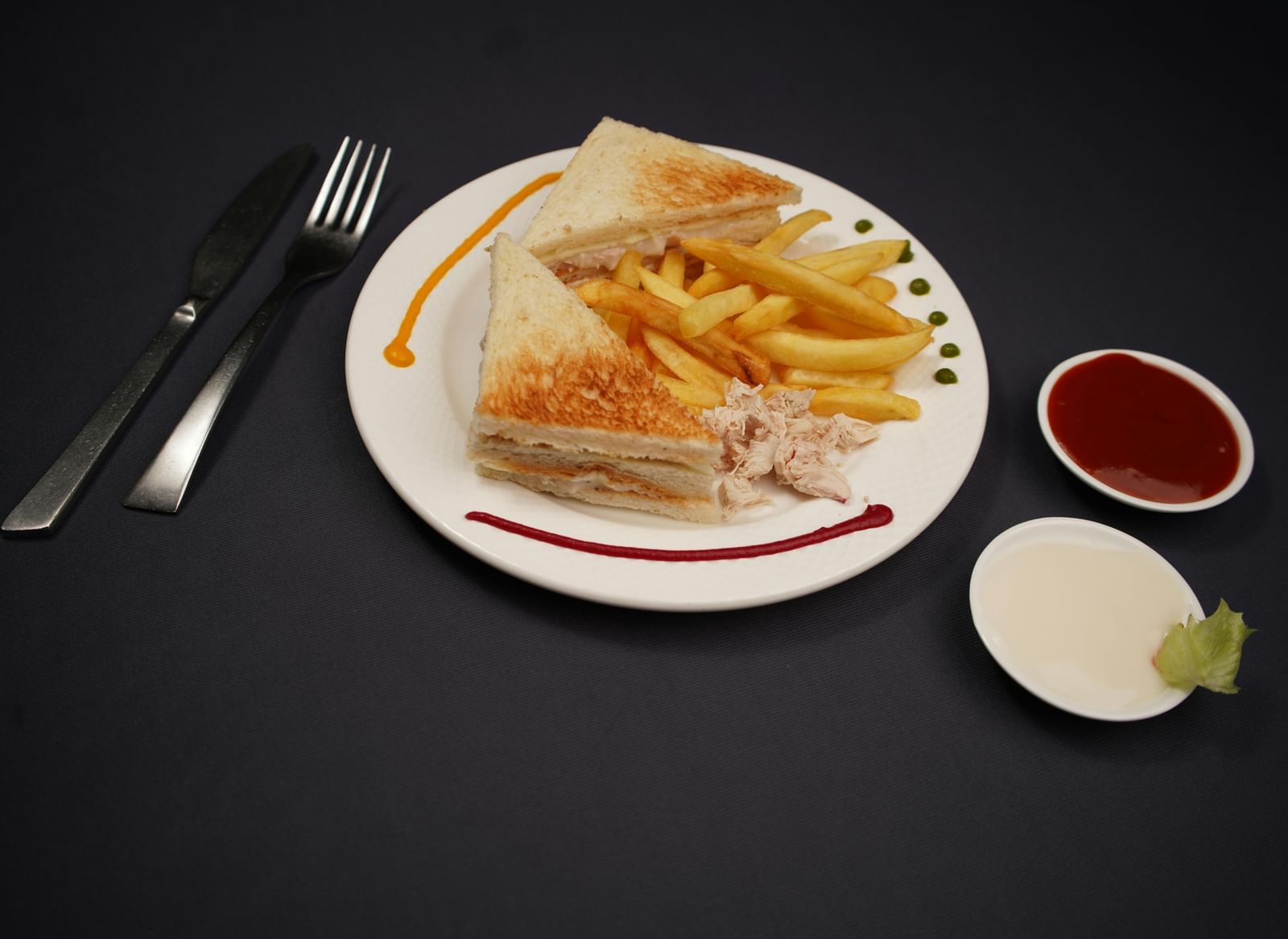 A plate of sandwich, is served with dipping sauces and a lime wedge on a dark surface.