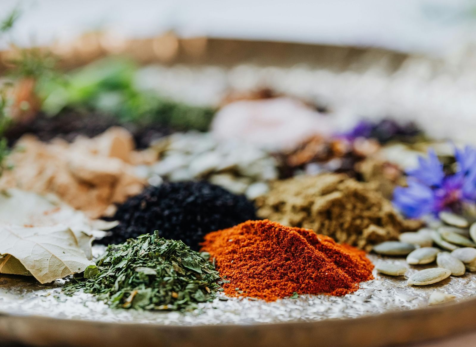  A variety of colorful spices and herbs arranged on a tray, showcasing their natural textures and vibrant colours.