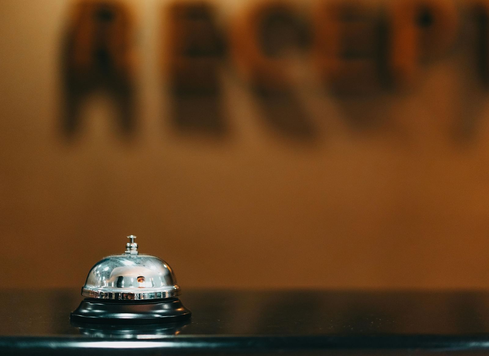 Reception bell at a hotel front desk with blurred ‘reception’ signage in the background.