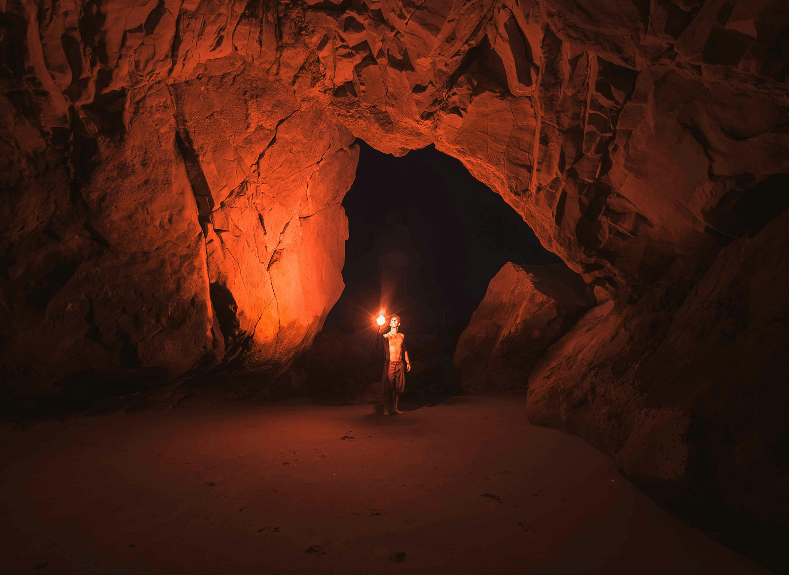 A man holding a red torch inside a cave.
