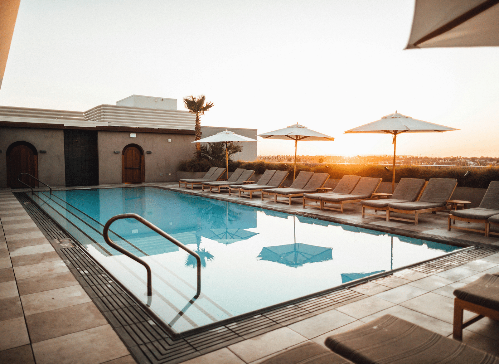 An image of a swimming pool featuring sun loungers seen during a sunset