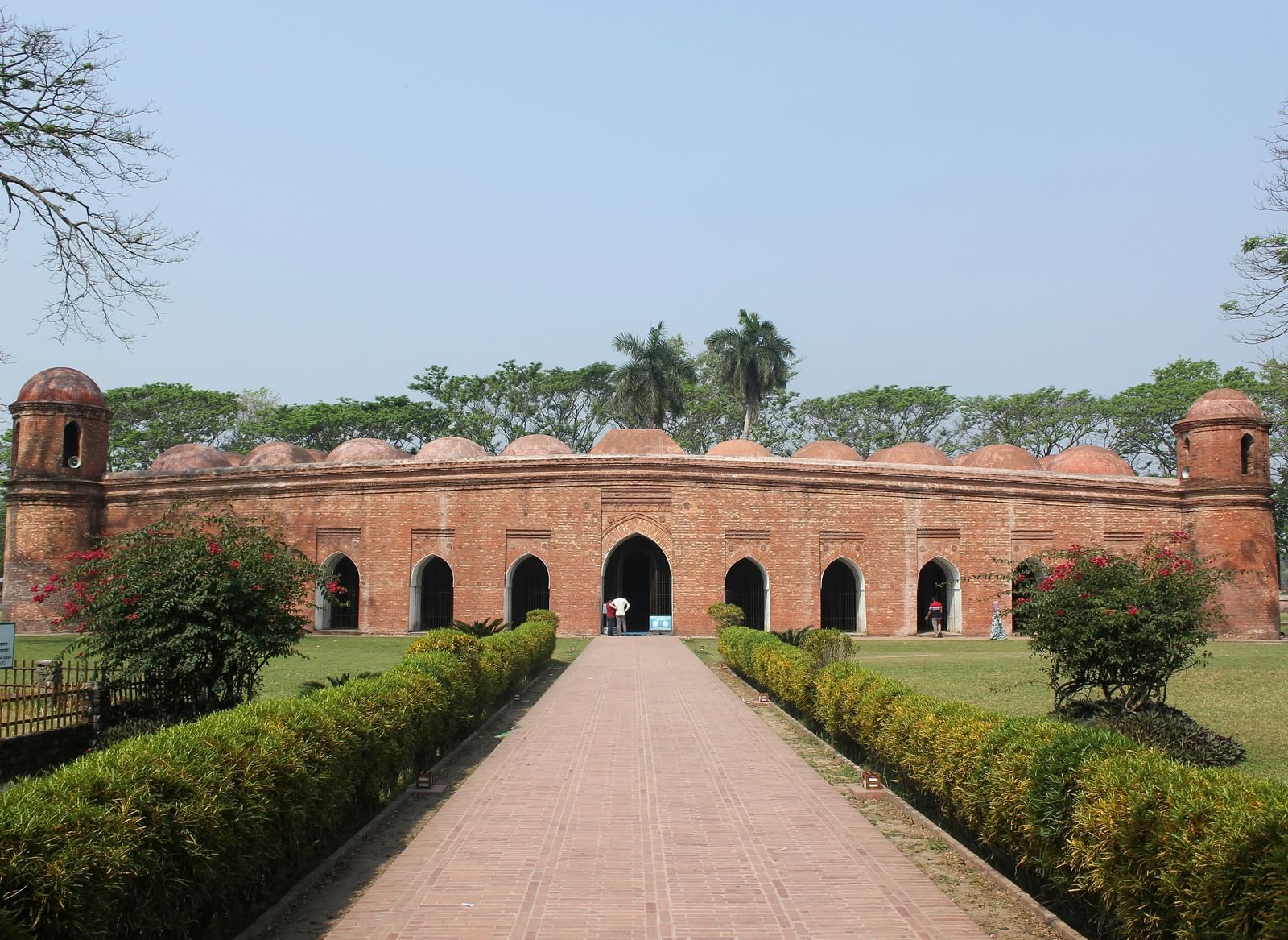 Historic brick fort or palace walls with a series of arches and a long manicured pathway.