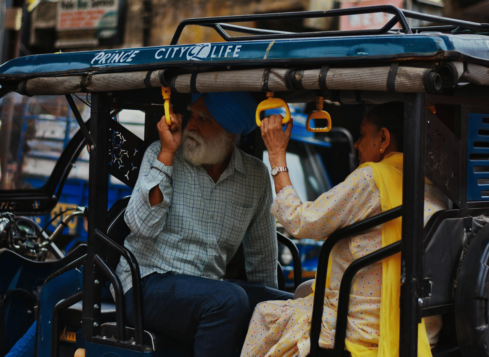 A bearded man and a young woman riding in the passenger section of a shared, covered three-wheeled auto rickshaw on a street.