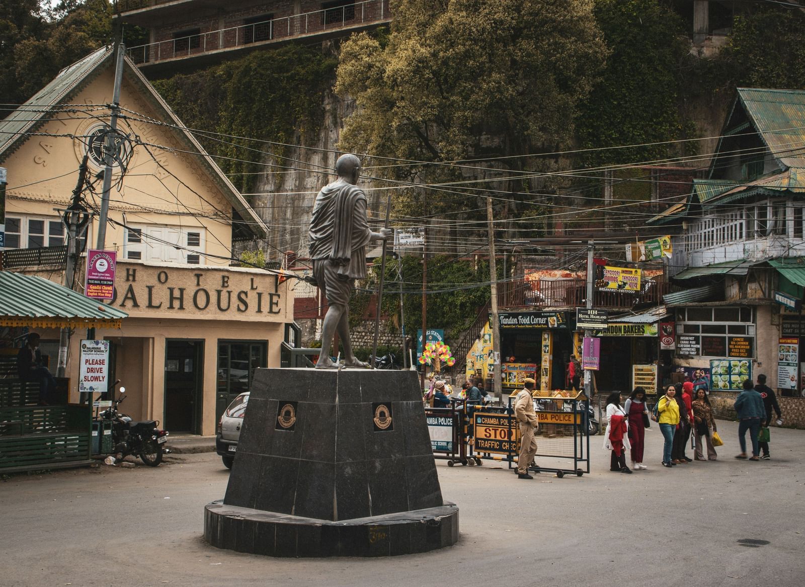 A busy square in a mountain village with old wooden buildings and people walking around a central statue.