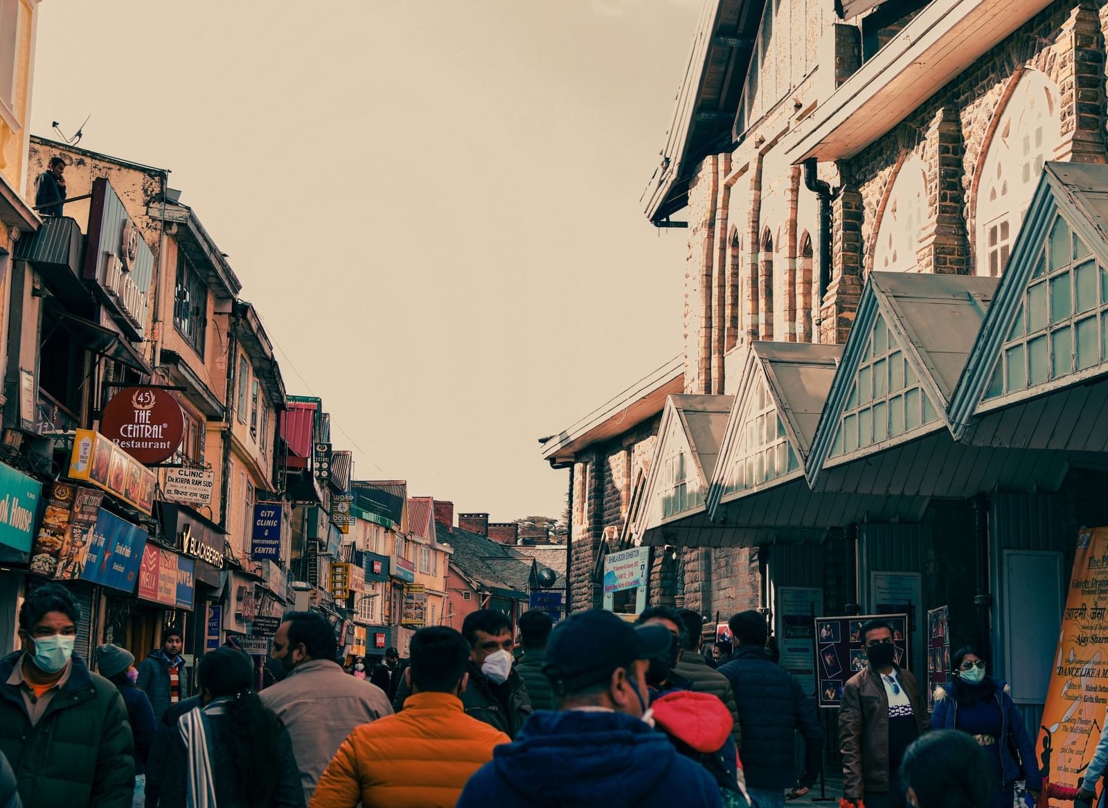A crowded street scene with people walking between old, multi-story buildings and street vendors.