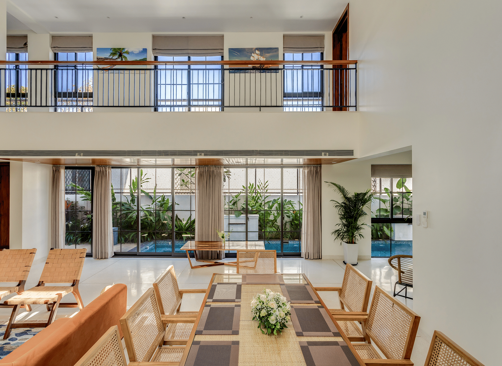 A bright dining area with a large wooden table and chairs, surrounded by floor-to-ceiling windows offering garden views - BluSalzz Villas - Alocassia, Anjuna