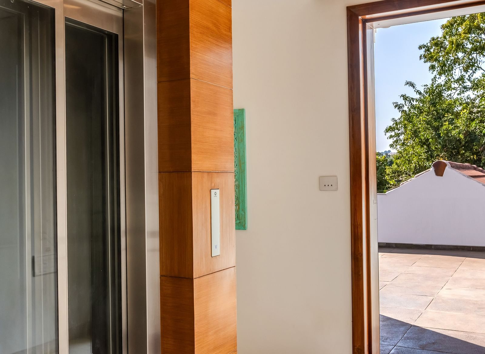 A corridor with wooden accents leading to a glass door that opens to an outdoor area under a clear blue sky - BluSalzz Villas - Alocassia, Anjuna