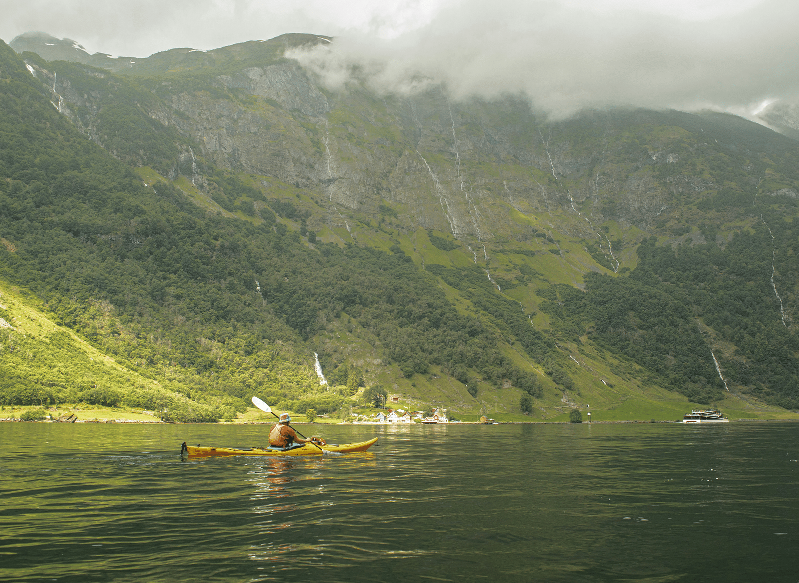  A person kayaking on a serene lake, with a lush, fog-covered mountain in the background.