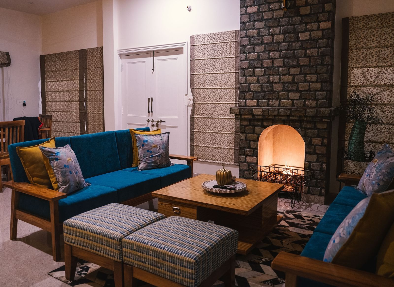 A living area with furniture arranged around a table by the fireplace at BluSalzz Villas - The Green Roof, Bhimtal.
