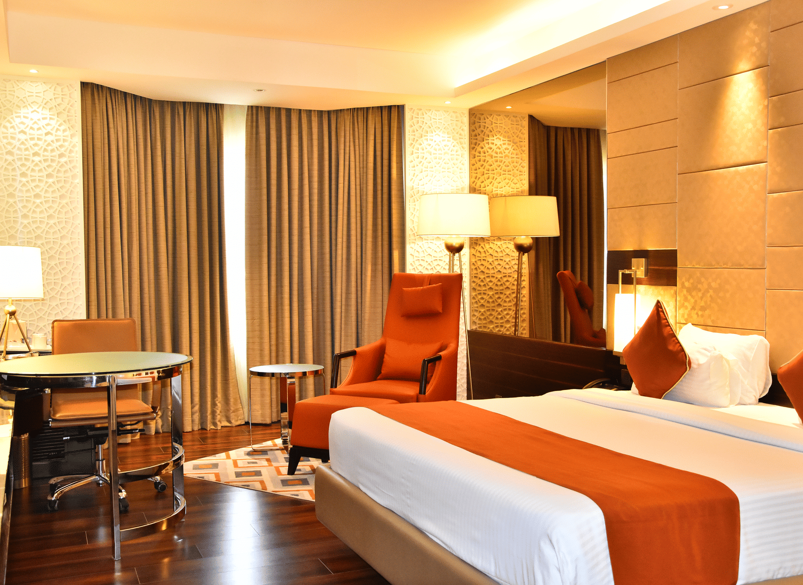 A spacious room with a large bed, a cushioned chair with a table beside it, and windows covered with curtains | Cenneys Gateway