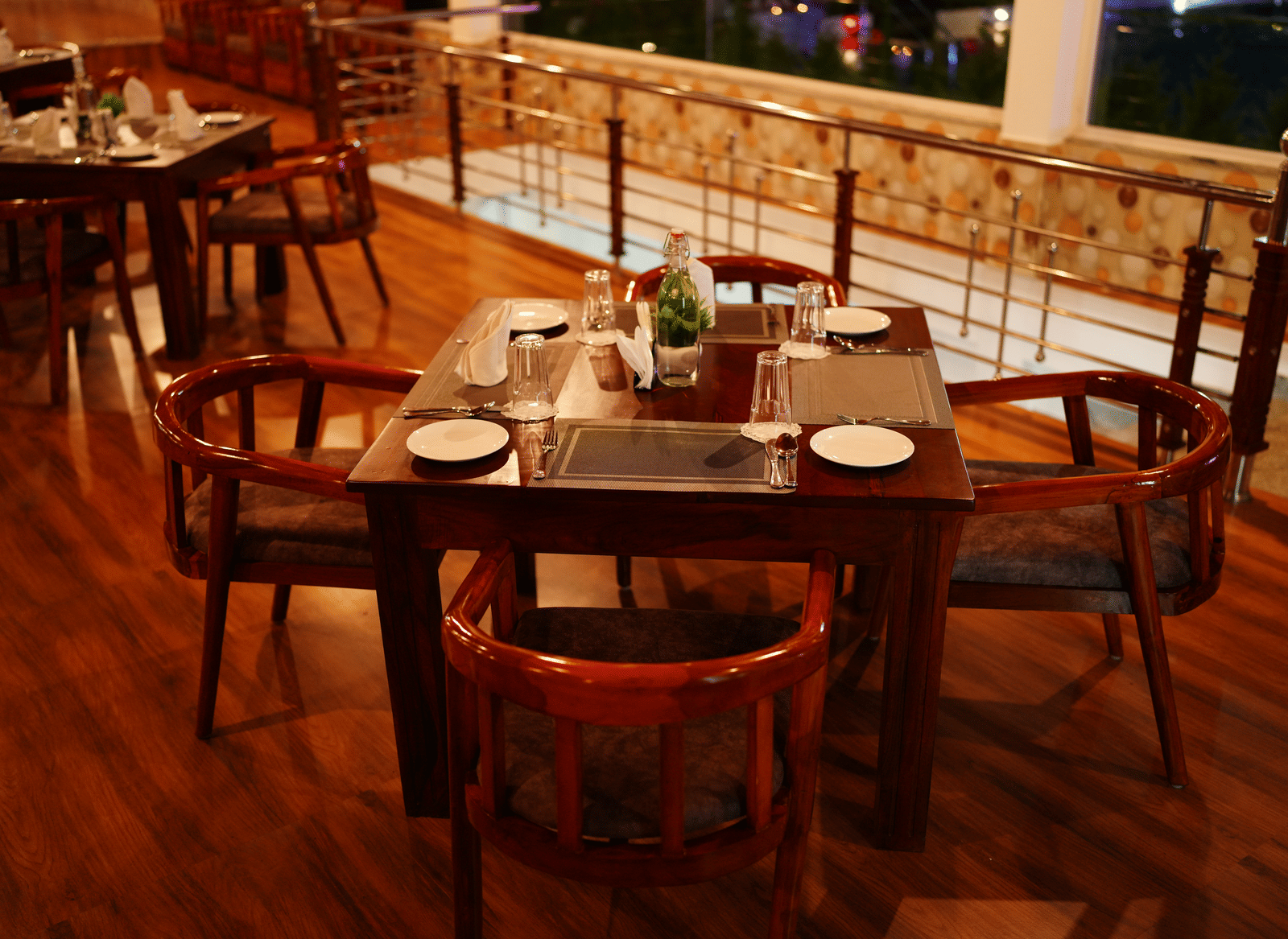 A close-up of a dark wooden dining table set with plates and cutlery in a dimly lit restaurant at Coorg Orange Blossom Resort and Spa.
