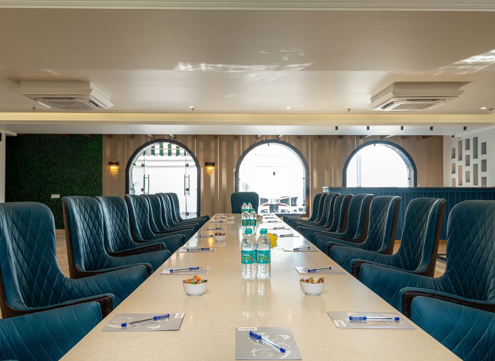 chairs arranged with a large table with notepads and pens along with water bottles on it as the daylight makes its way through the windows in the background