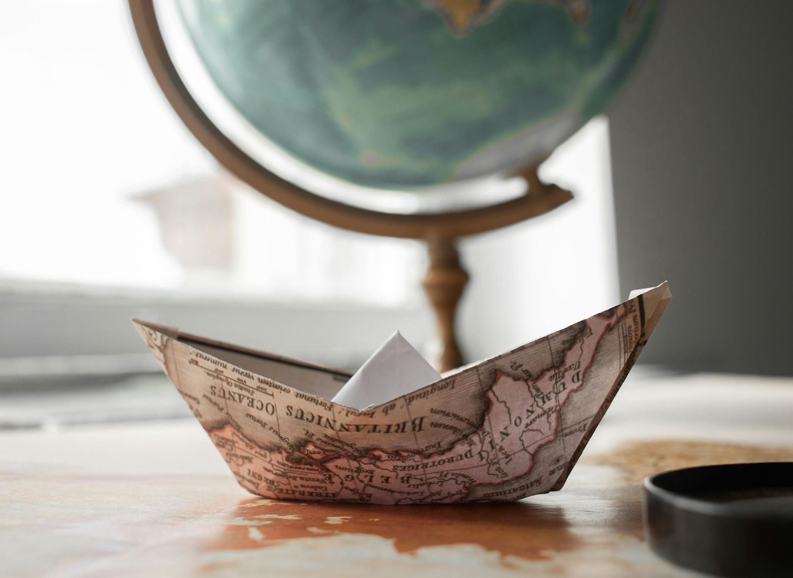 a paper boat made from a map, with a globe in the background
