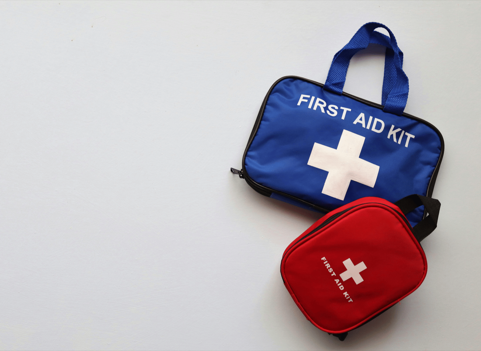 A flat lay composition featuring 2 fabric first aid kit bags, each marked with a cross symbol, positioned against a plain background.
